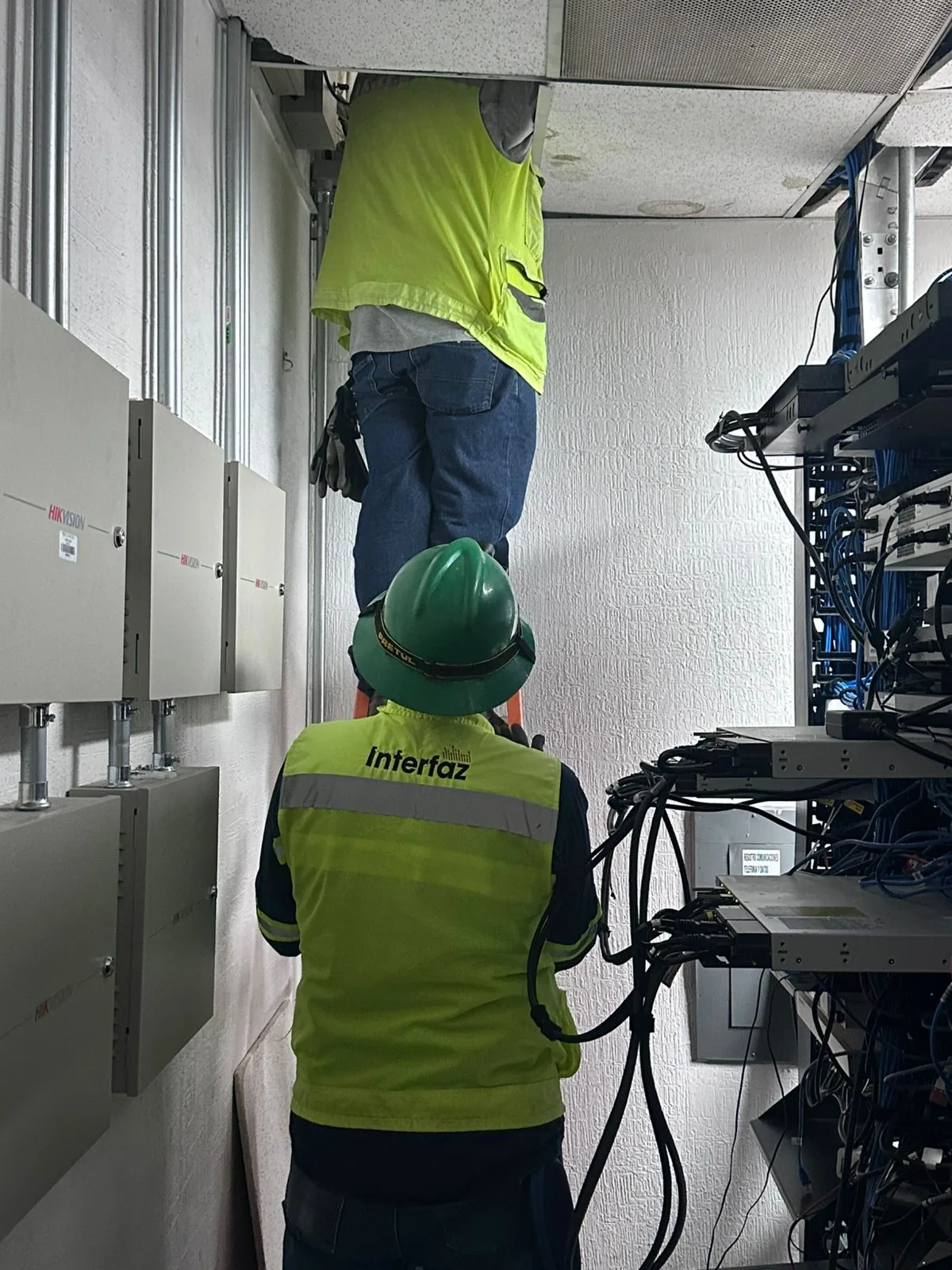 Técnicos de Interfaz trabajando en un cuarto de telecomunicaciones, uno de ellos sobre el plafón